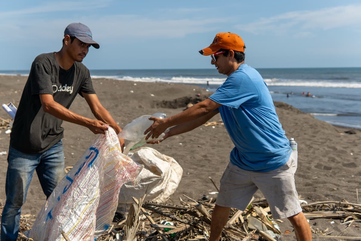 Two Tidey Ocean volunteers passing bags of collected plastic