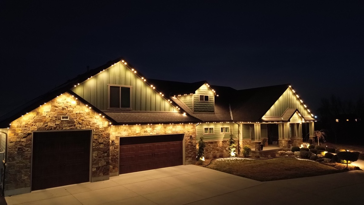Warm white permanent accent lighting on a stone and siding home in Salt Lake City with landscape lighting at dusk